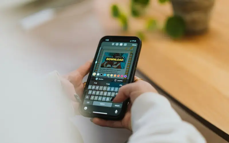 Hands holding a smartphone showing a game download screen, illustrating the EM777PH app download