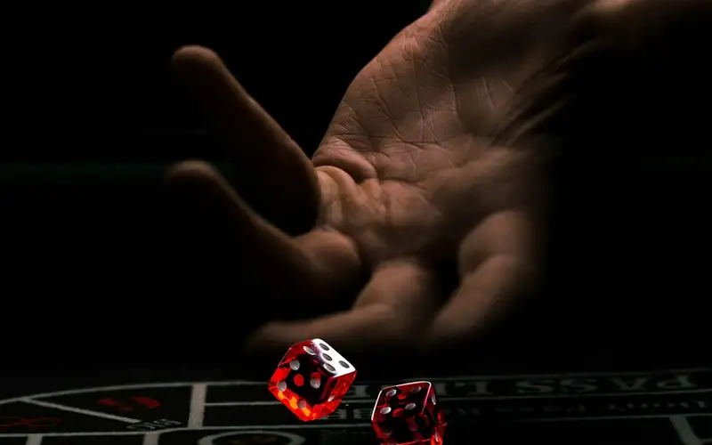 A hand tossing two red dice onto a dark casino table at night