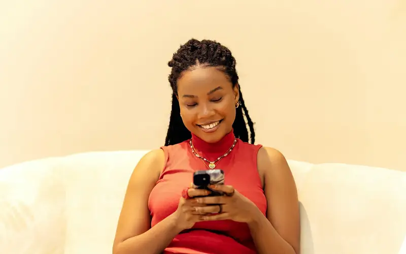 Smiling young woman relaxing on a sofa while using her smartphone, the way many Filipino players enjoy EM777PH on mobile
