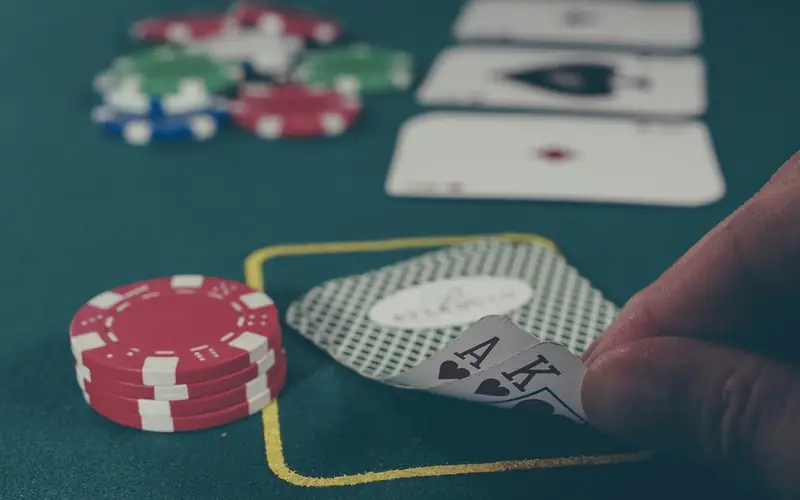 Player lifting an ace and king of spades on a green poker table next to casino chips